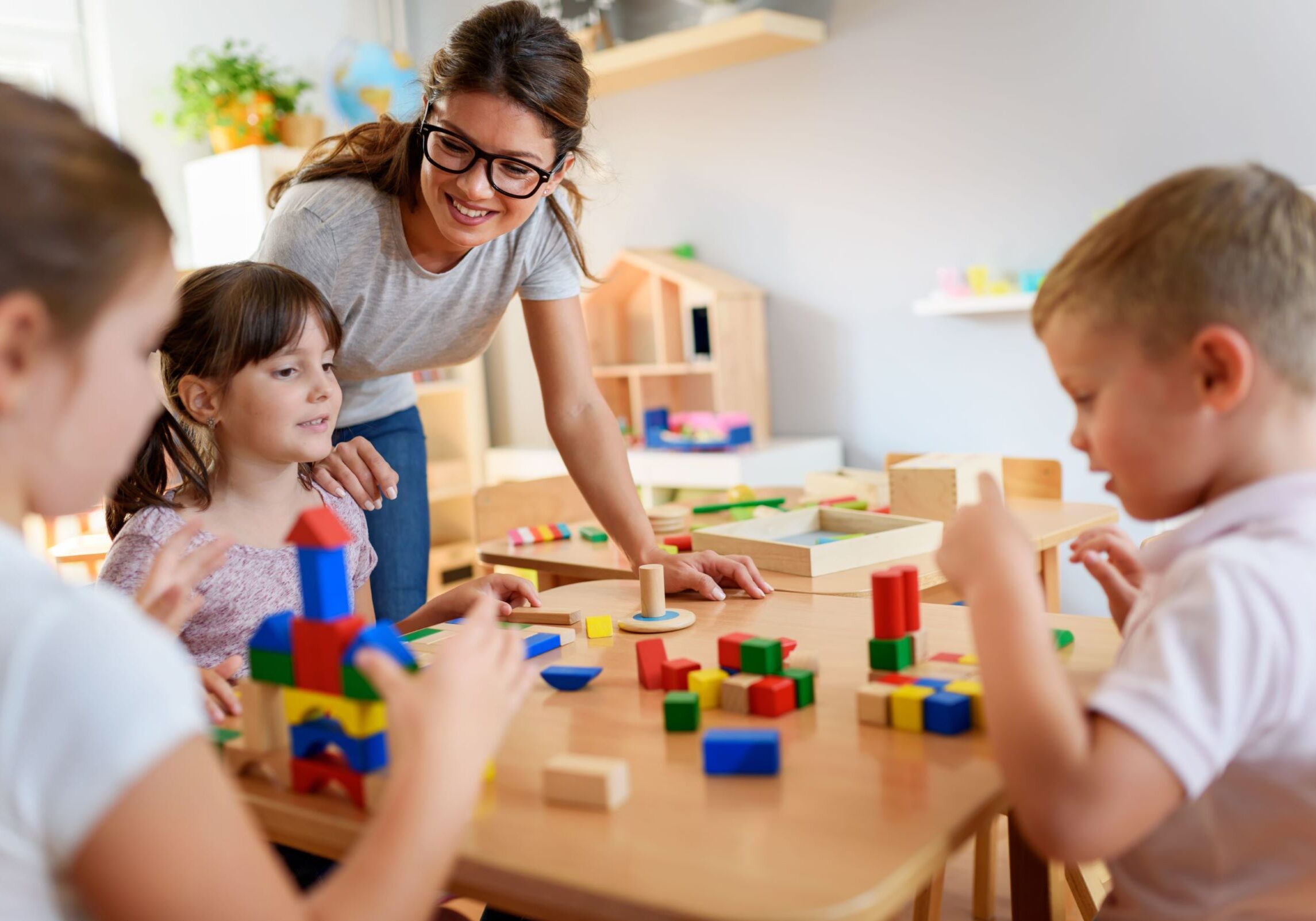 Teacher and two children playing with colorful wooden blocks at a table