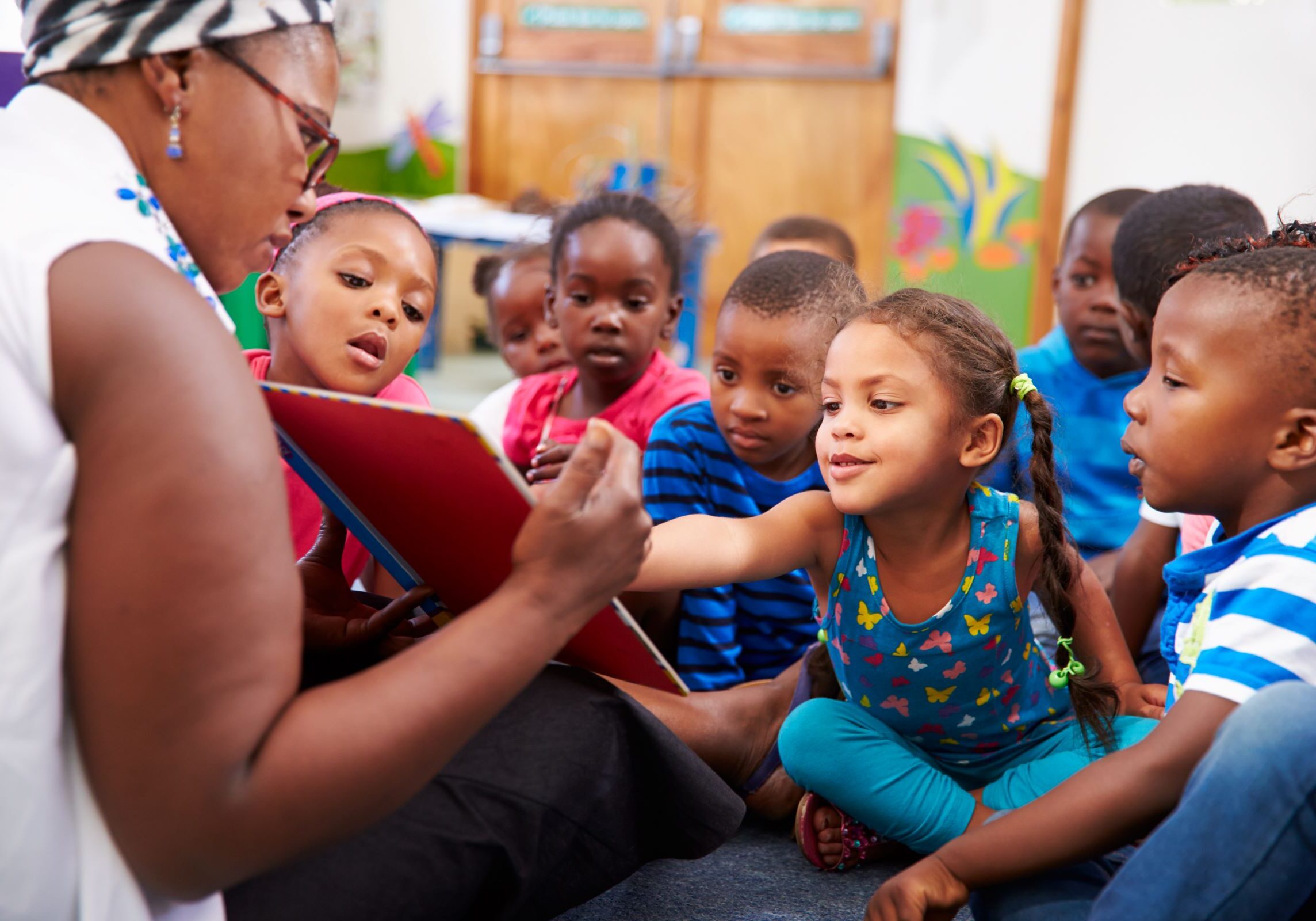 Teacher using a tablet to show an interactive story to an engaged group of preschool students.