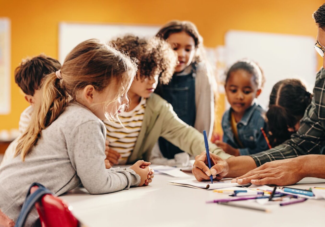 Teacher and young children drawing together at a classroom table.