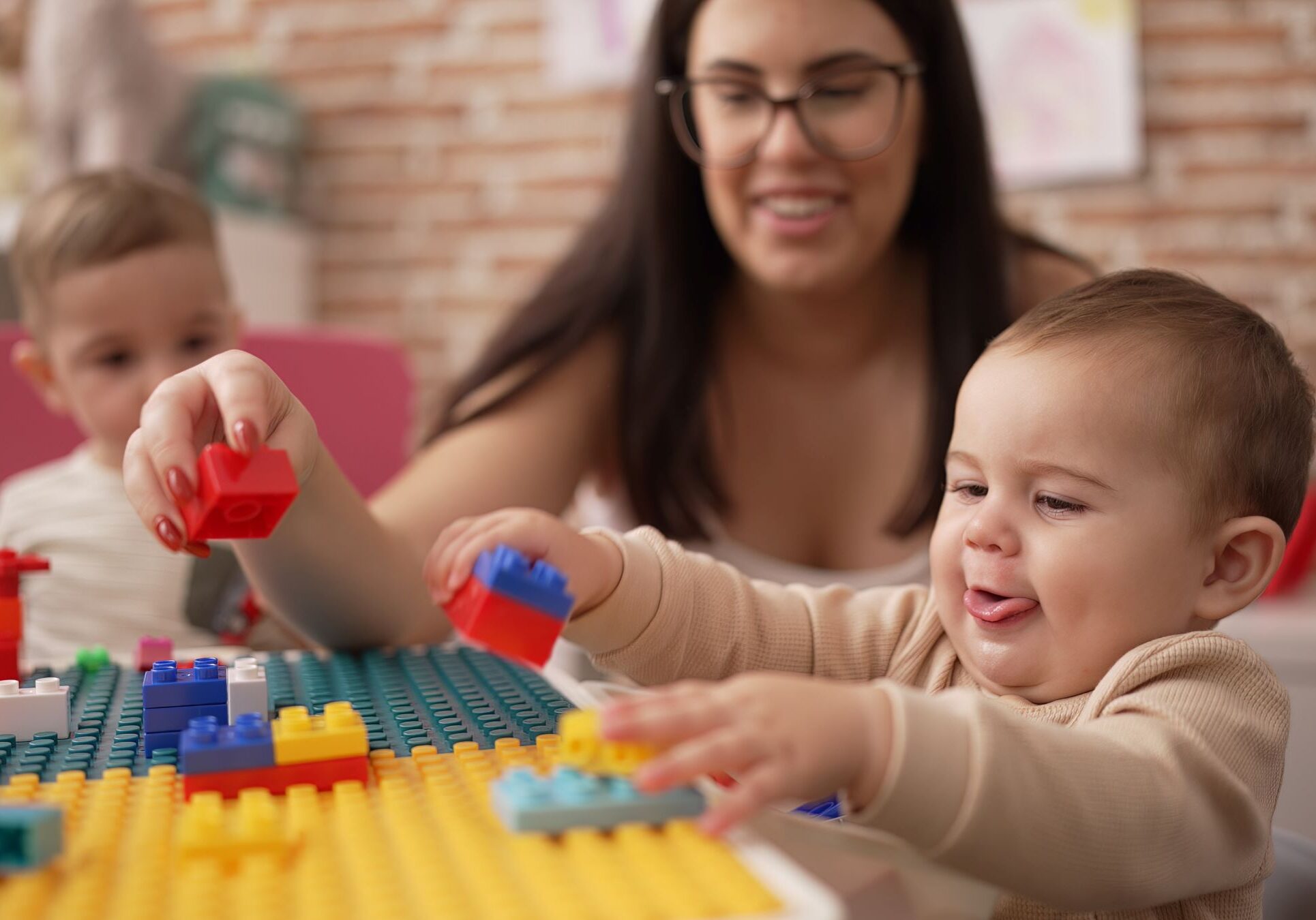 Teacher and preschool students playing with construction blocks sitting on table at kindergarten